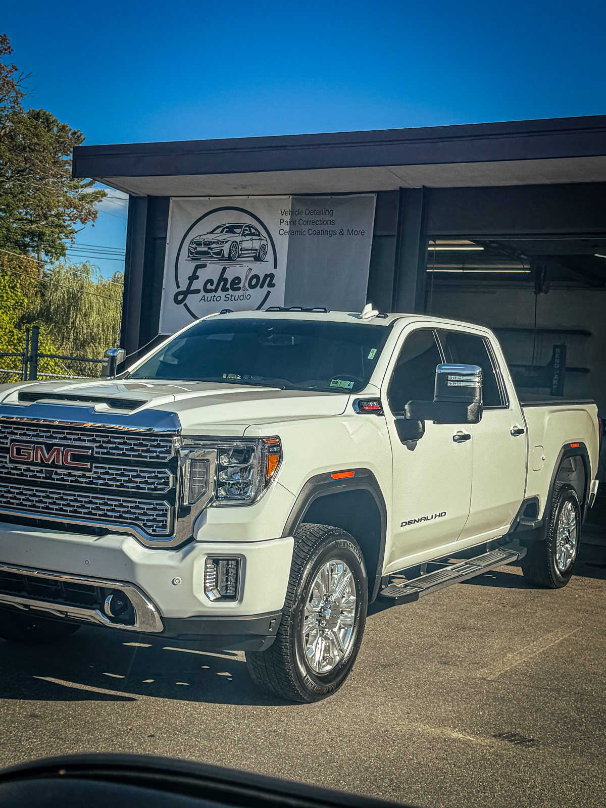 White GMC Sierra Denali HD in front of the Echelon Auto Studio banner